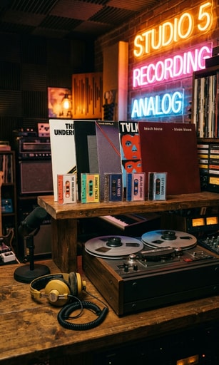 Five vinyl records and cassettes curated in a warm indie music studio.